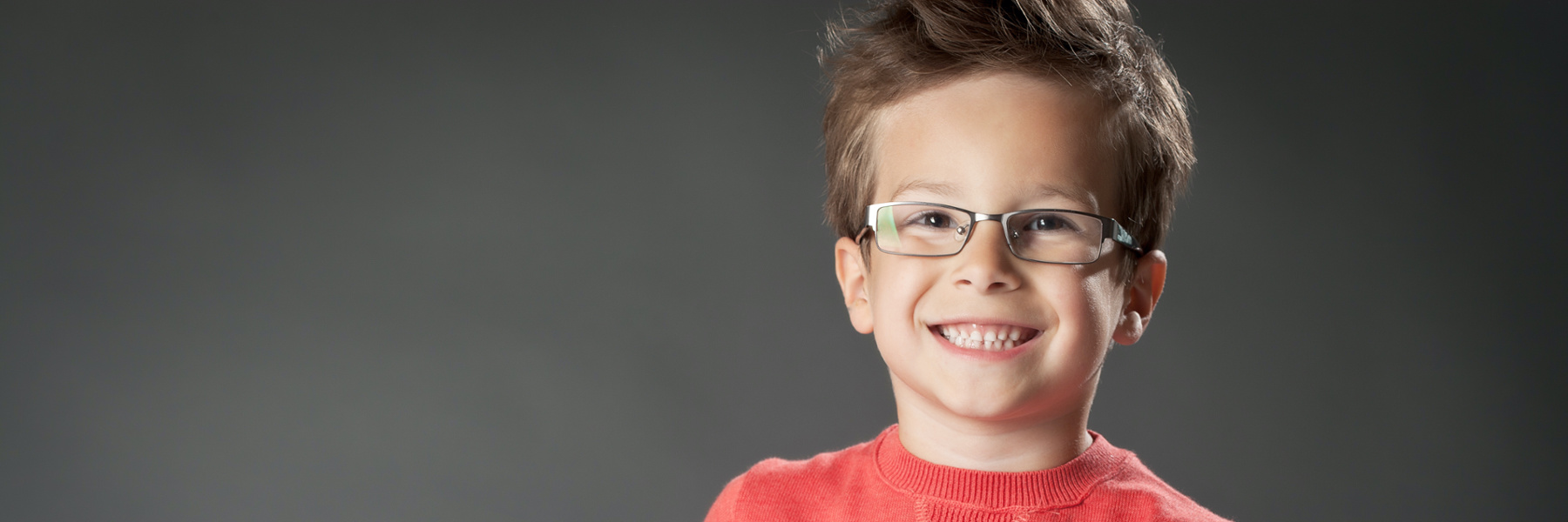Happy young boy with glasses wearing red sweater showing bright healthy smile near Lifetime Dental