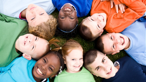 Diverse group of children lying in circle on grass displaying bright healthy smiles in Prahran