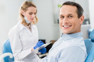 Smiling patient in a dentist chair with dentist in the background